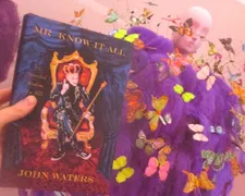 Mr. Know-It-All by John Waters (out on May 21, Farrar Straus & Giroux) in front of Jeremy Scott dress for House of Moschino