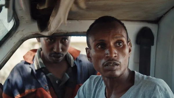 Ivory dealer "X" (outside car window) and poacher Lukas wait for the wildlife rangers to pass in When Lambs Become Lions
